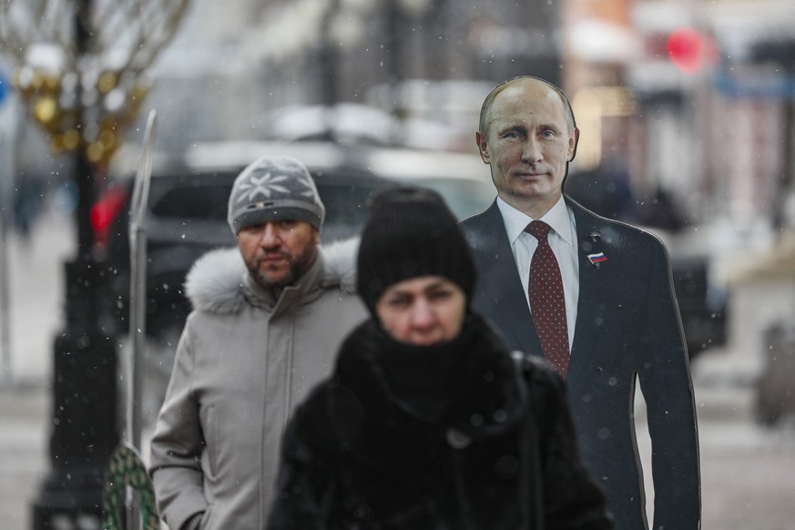 epa11015299 People pass by a cardboard cutout of Russian President Vladimir Putin on a street in downtown Moscow, Russia, 07 December 2023. The Federation Council adopted a resolution calling for a pr ...