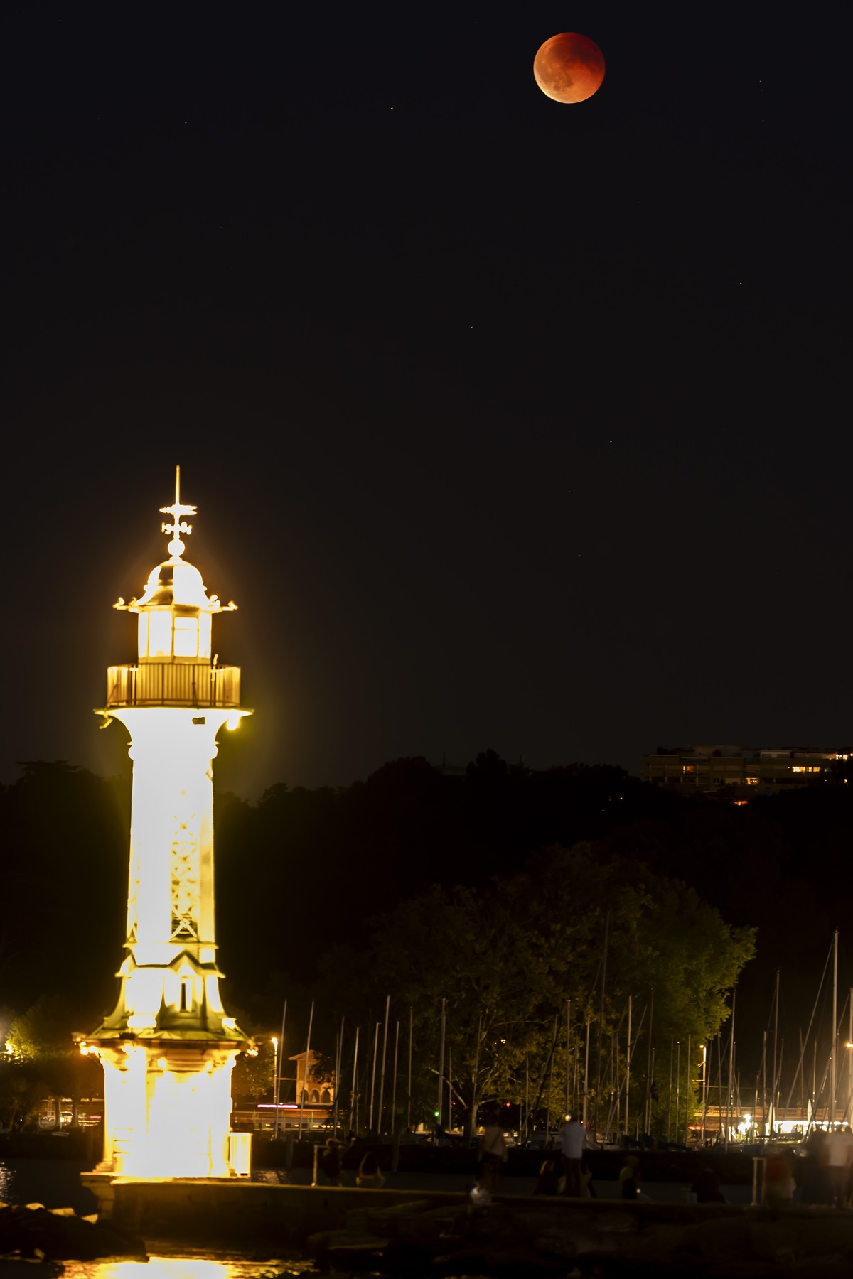 epa12360743 The Blood Moon is seen behind the lighthouse at the Bains des Paquis during a total lunar eclipse in the sky over of Geneva, Switzerland, 07 September 2025. EPA/SALVATORE DI NOLFI