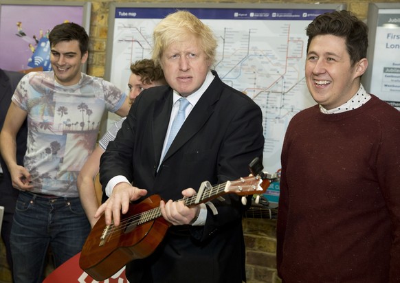 FILE - In this Monday, March 23, 2015 file photo Mayor of London Boris Johnson plays with a guitar in front of the busking band The Tailormade during a photocall to promote two new schemes aimed at su ...
