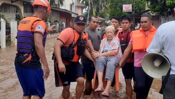 epa10379152 A handout photo made available by the Philippine Coast Guard (PCG) shows coast guard personnel carrying an elderly woman at a flooded road in the town of Plaridel, Misamis Occidental provi ...