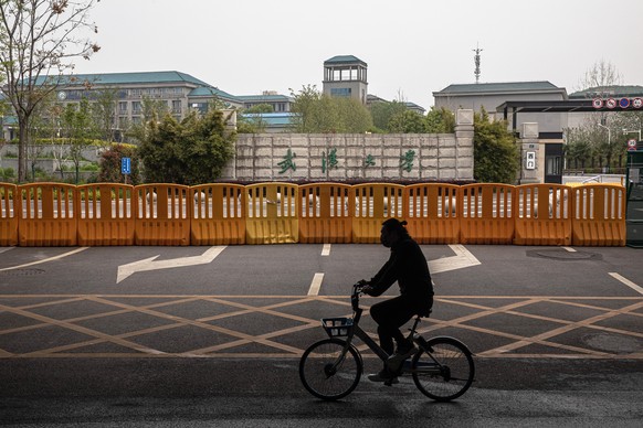 epa08338268 A man wearing a protective face mask rides a bicycle next to a security fence surrounding territory of Wuhan University, in Wuhan, China, 02 April 2020. Many students in Wuhan&#039;s unive ...