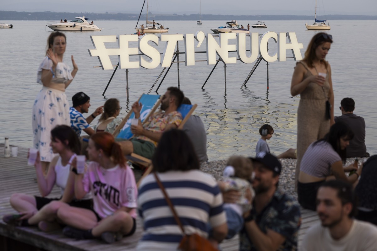 Des personnes profitent de l'ambiance au bord du lac devant le logo du festival neuchatelois lors du festival openair Festi'Neuch ce samedi 14 juin 2025 a Neuchatel. Festi'neuch, Neucha ...