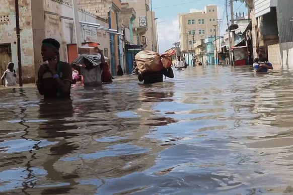 In this image taken from a video, men walk through floodwaters on a street in the town of Beledweyne, Somalia, on Sunday, November 19, 2023. First, some families fled drought and violence.  Now they say they...