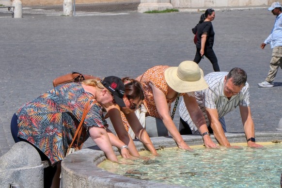Eine Gruppe von Touristen kühlt sich an einem Brunnen in Rom ab.