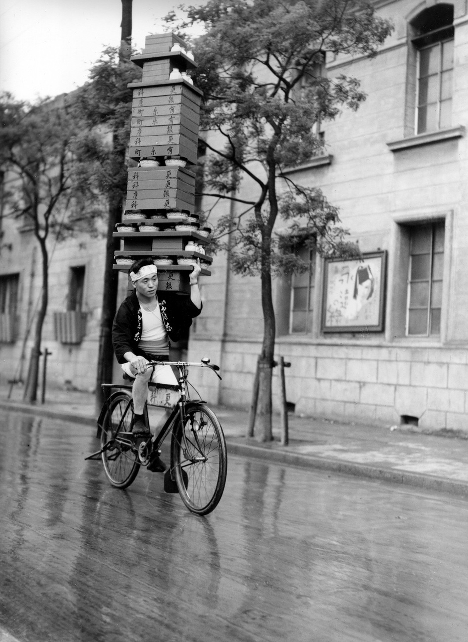 A delivery man for a Tokyo restaurant maneuvers his bicycle as he balances on his shoulder a high stack of trays containing soba bowls through a street in Japan on March 8, 1937. (AP Photo)