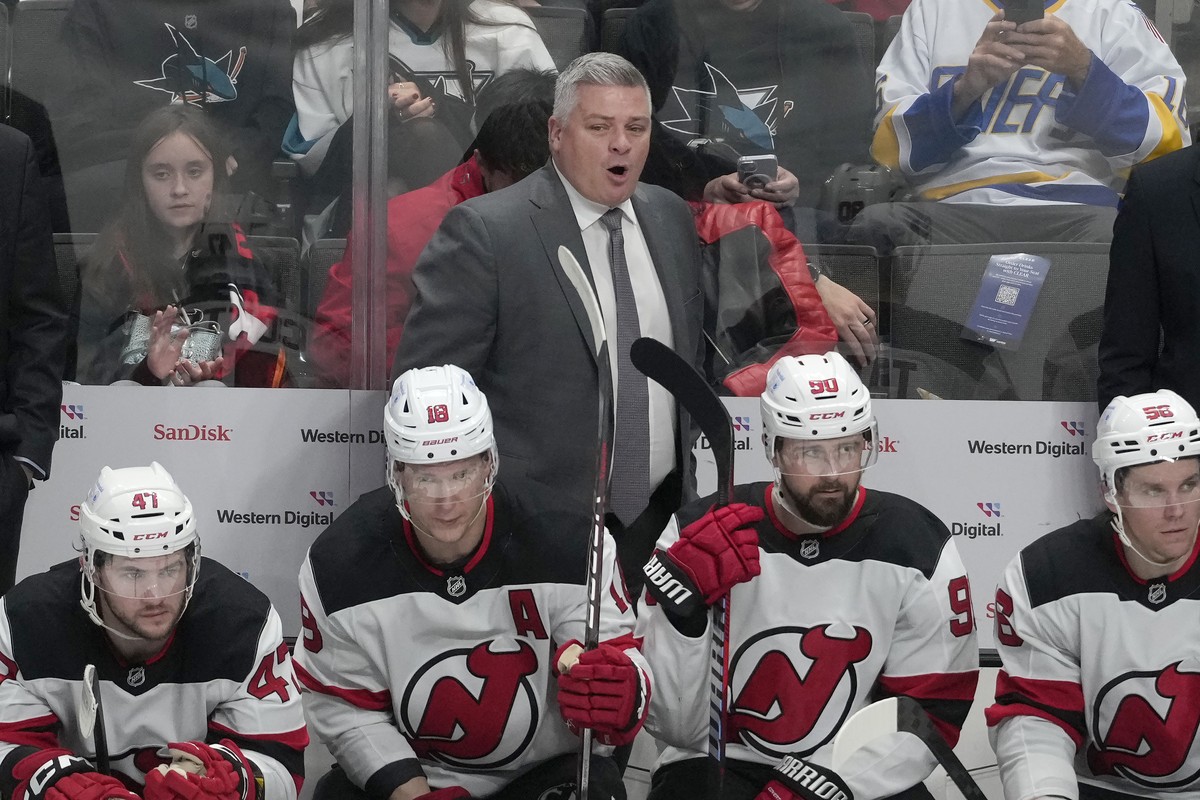 New Jersey Devils head coach Sheldon Keefe, standing, watches from behind players on the bench during the third period of an NHL hockey game against the San Jose Sharks in San Jose, Calif., Saturday,  ...