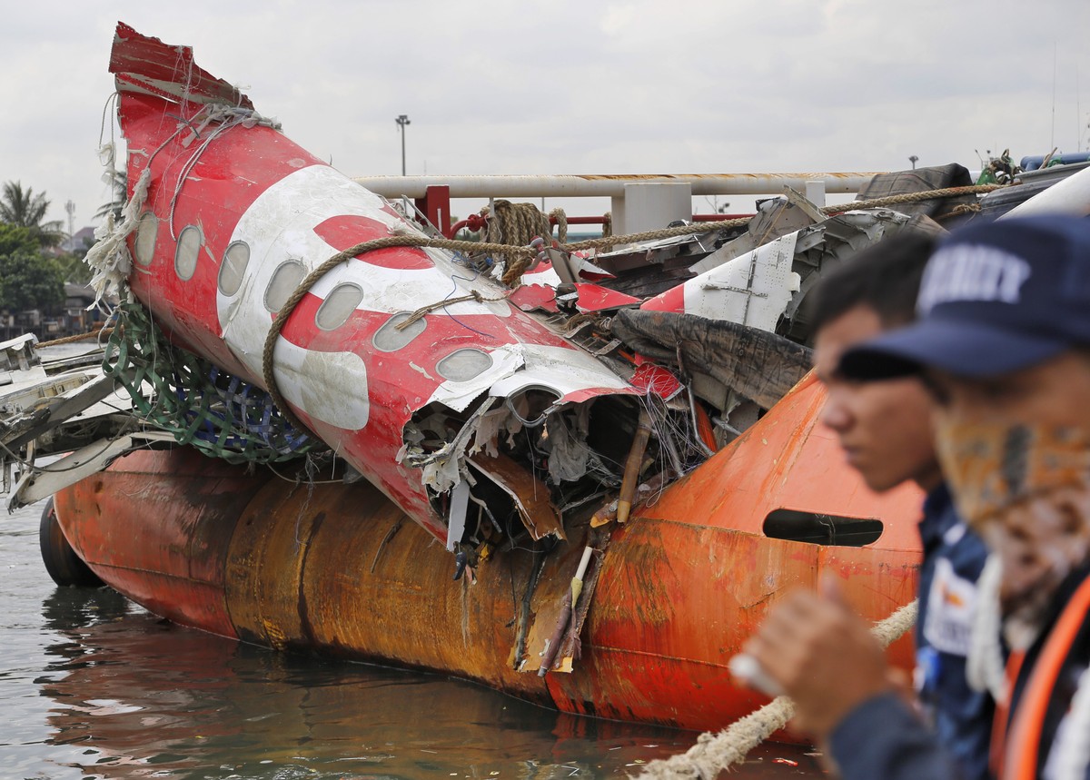 Security guards stand near the newly-recovered remains of the fuselage of the ill-fated AirAsia Flight 8501 on the deck of rescue ship Crest Onyx at Tanjung Priok port in Jakarta, Indonesia, Monday, M ...