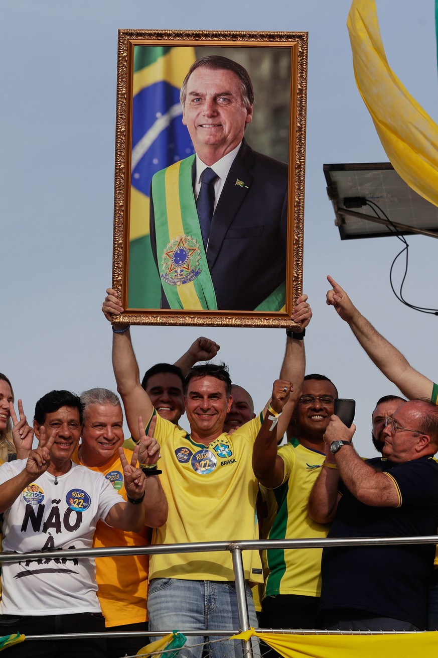 Opposition presidential candidate Flavio Bolsonaro holds a photo of his father, former President Jair Bolsonaro, as he rides a boat during a campaign rally ahead of the October general election in Ang ...