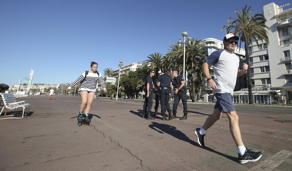 French police officers gather while people jog on the Promenade des Anglais near the scene of a truck attack in Nice, southern France, Saturday, July 16, 2016. Nice&#039;s seaside boulevard reopens to ...