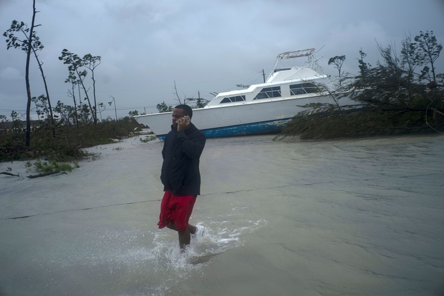 A man talks on his mobile phone next to a catamaran that was thrown onshore by the Hurricane Dorian near highway close Freeport, Grand Bahama, Bahamas, Tuesday Sept. 3, 2019. Relief officials reported ...