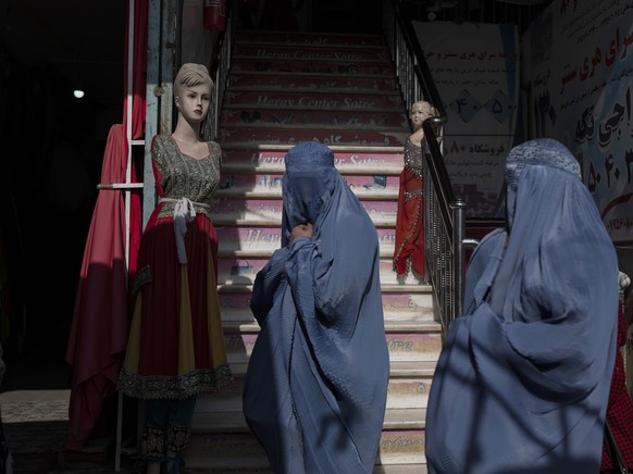 Burka-wearing Afghan women walk past a clothing shop, in Herat, Afghanistan, Tuesday, Nov. 23, 2021. (AP Photo/Petros Giannakouris)