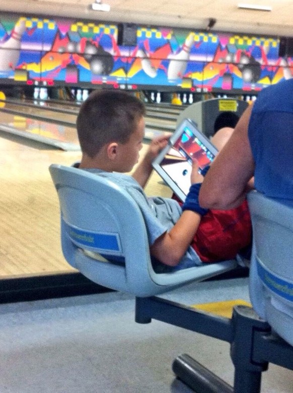Ein Kind spielt iPad-Bowling im Bowling-Center. Gut gemacht, Eltern!