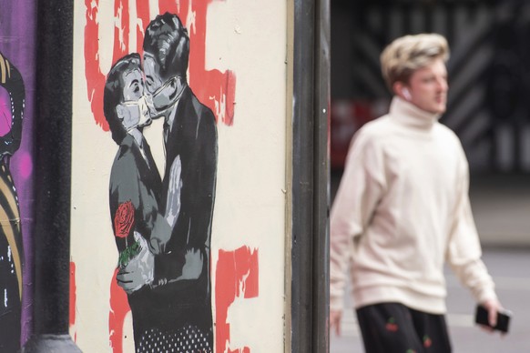 A man passes a poster showing a couple wearing protective face masks embracing in Shoreditch area of east London, following the introduction of measures to bring England out of the coronavirus lockdow ...