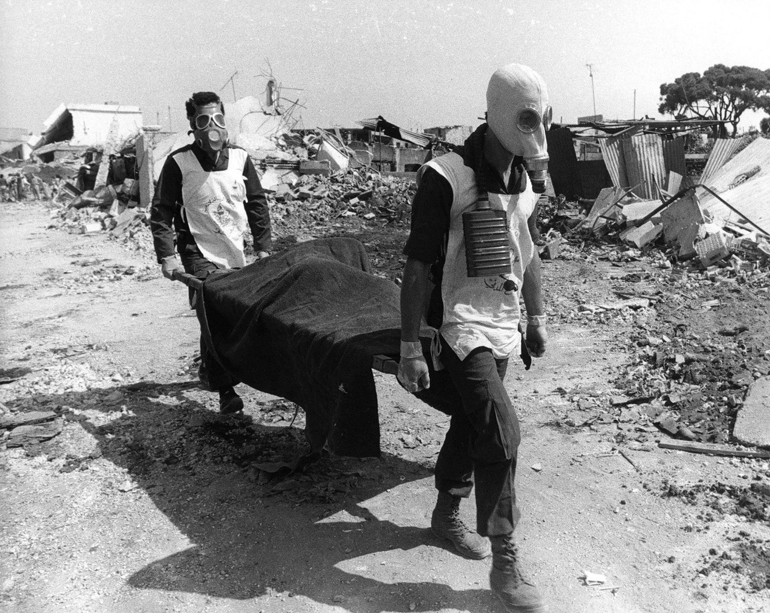 Zivilschutzangestellte mit Gasmasken tragen die Leiche eines Opfers des Massakers von Sabra und Chatila weg vom zertruemmerten Schauplatz des Ueberfalls, am 19. September 1982 in Sabra bei Beirut. Am  ...
