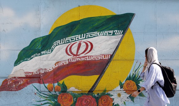 epa10295546 A woman walks past a graffiti showing the Iranian national flag in Tehran, Iran, 09 November 2022. Iran has been rocked by anti-government protests, with supporters worldwide, following th ...