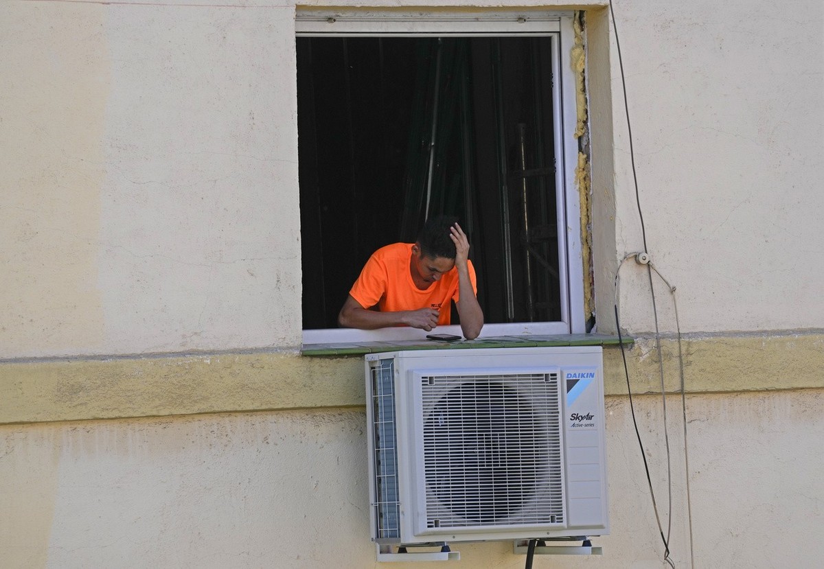 A worker looks at his phone during a break by a newly installed air conditioner unit fixed outside an apartment in Madrid, Spain, Wednesday, April 26, 2023. Spain is experiencing summer temperatures i ...