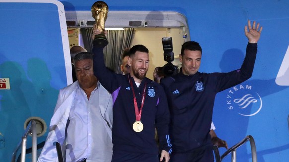 epa10374424 Lionel Messi (C) of the Argentina national soccer team descends a plane with the trophy of Qatar 2022 World Cup accompanied by head coach Lionel Scaloni (R), upon ther arrival to the Inter ...