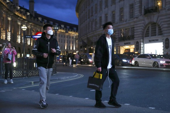 Two pedestrians cross the street wearing masks in Piccadilly Circus, London, Saturday, March 14, 2020. British Prime Minister Boris Johnson has described the worldwide pandemic as Ã¢??the worst public ...