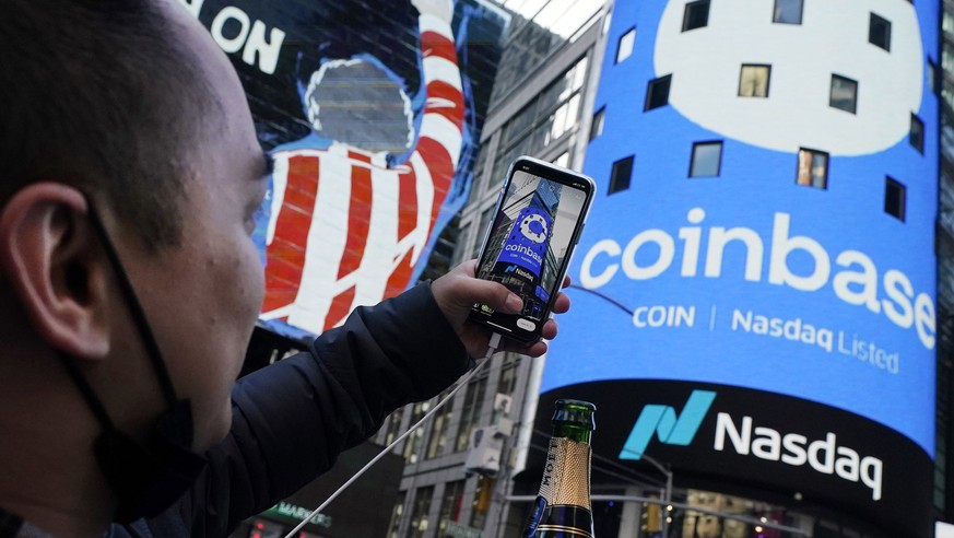 FILE - Coinbase employee Daniel Huynh holds a celebratory bottle of champagne as he photographs outside the Nasdaq MarketSite, in New York&#039;s Times Square, April 14, 2021. Coinbase rose, Friday, J ...
