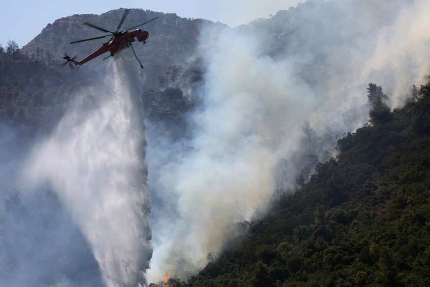 epa09403610 A firefighting helicopter douses a wildfire in Malakassa area, near Athens, Greece, 07 August 2021. Substantial firefighting forces are still battling against fire rekindlings in northern ...