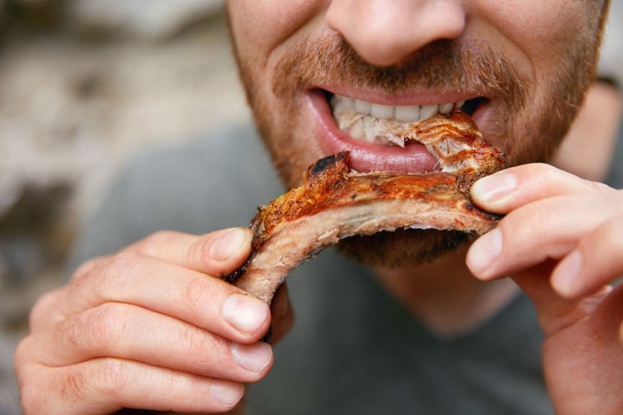 Ein Mann beisst in ein Stück Spareribs.