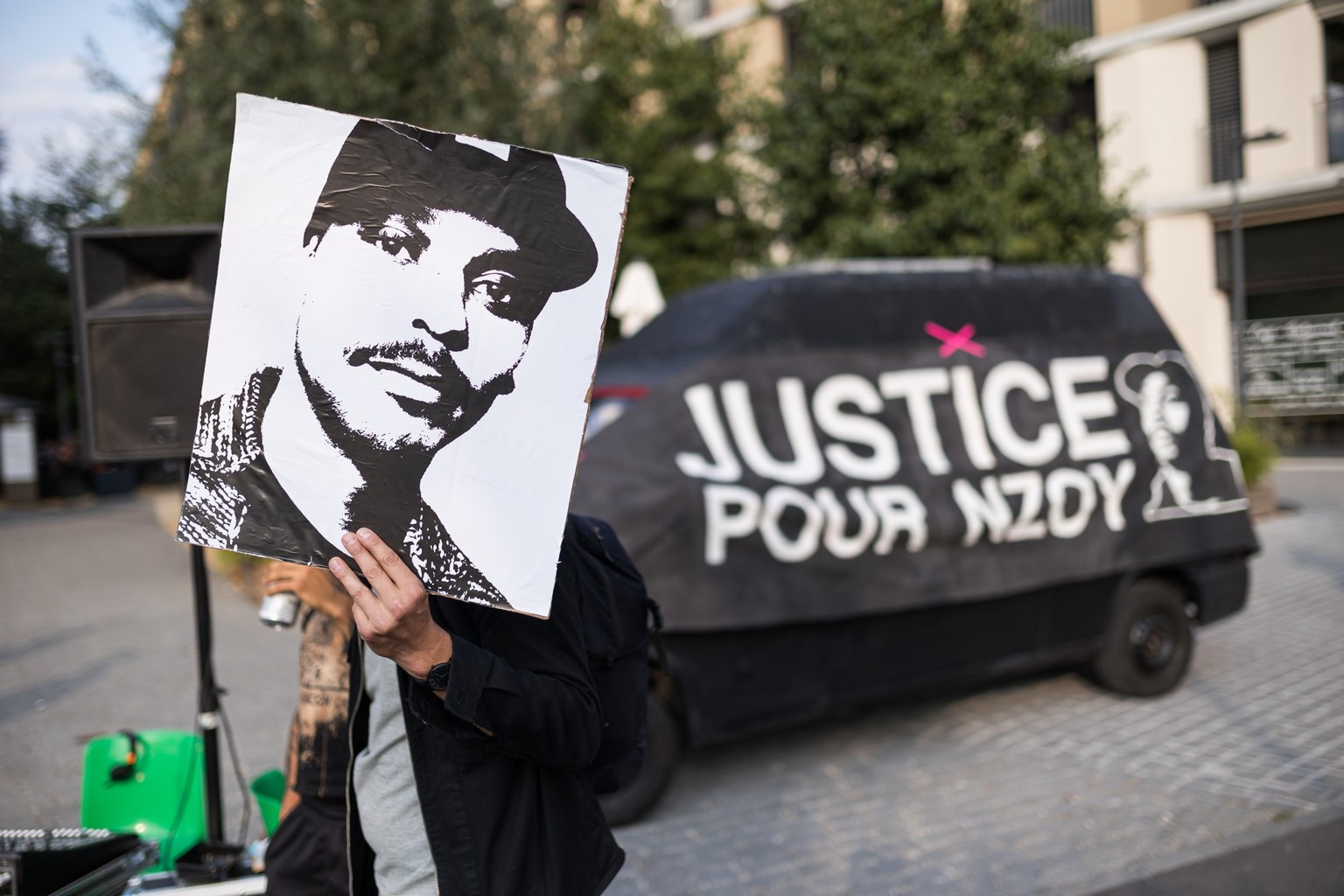Une personne tient un portrait de Nzoy devant une banderole � justice pour Nzoy � lors d&#039;un rassemblement devant l&#039;entree de la gare CFF de Morges a la memoire de Nzoy, tue par balle par un  ...