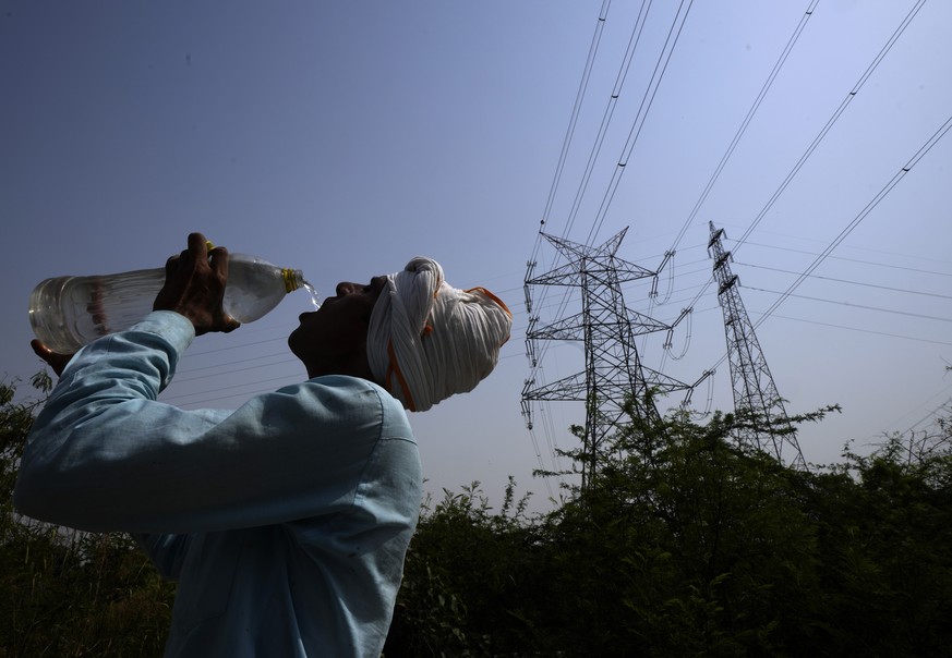 A workers quenches his thirst next to power lines as a heatwave continues to lashes the capital, in New Delhi, India, Monday, May 2, 2022. An unusually early and brutal heat wave is scorching parts of ...