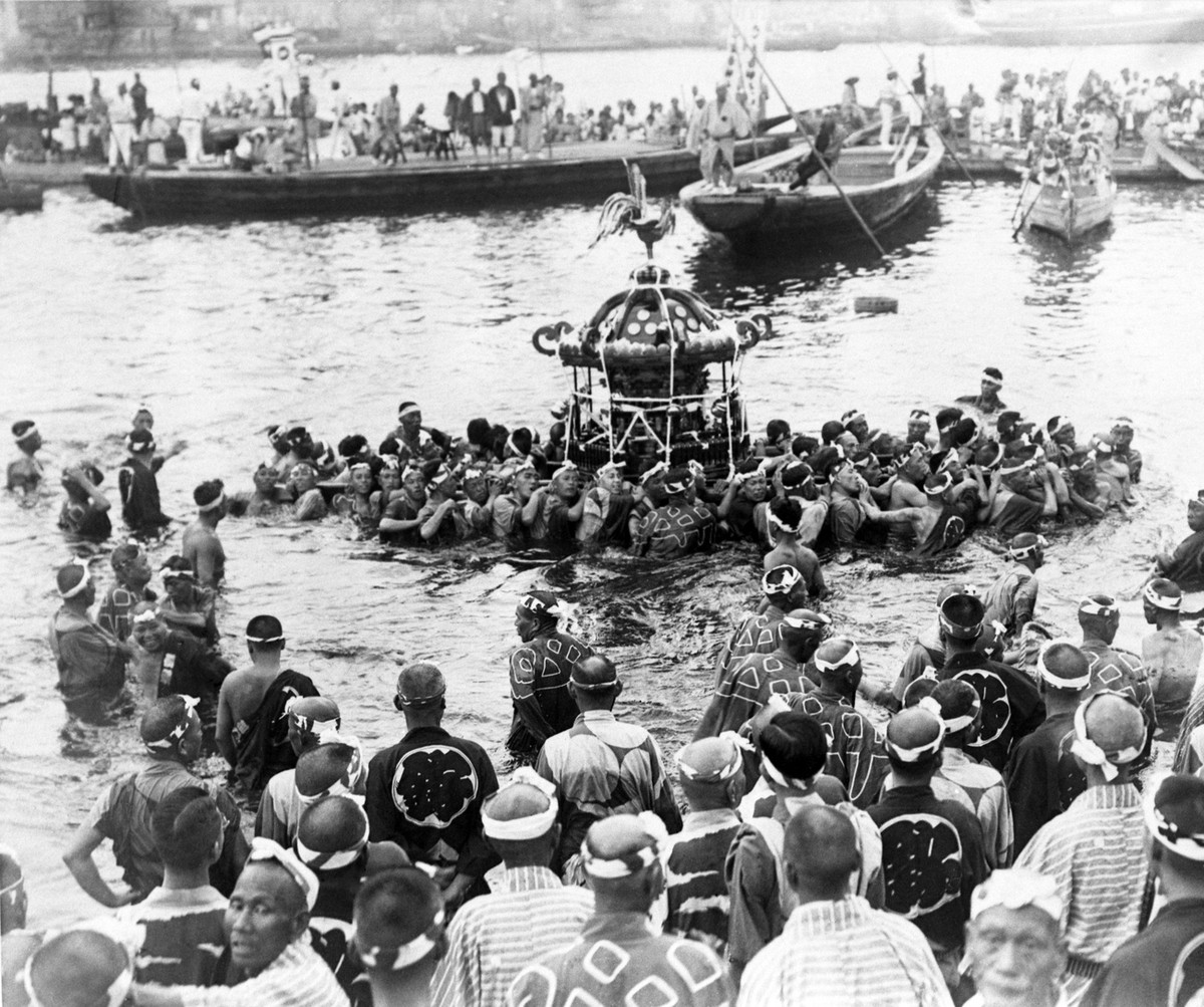 View of the ancient mid-Summer festival of the Tsukuda Shrine showing fisherman carrying the Mikoshi across the river to Tokyo's water-front, witnessed by spectators gathered around in boats on S ...