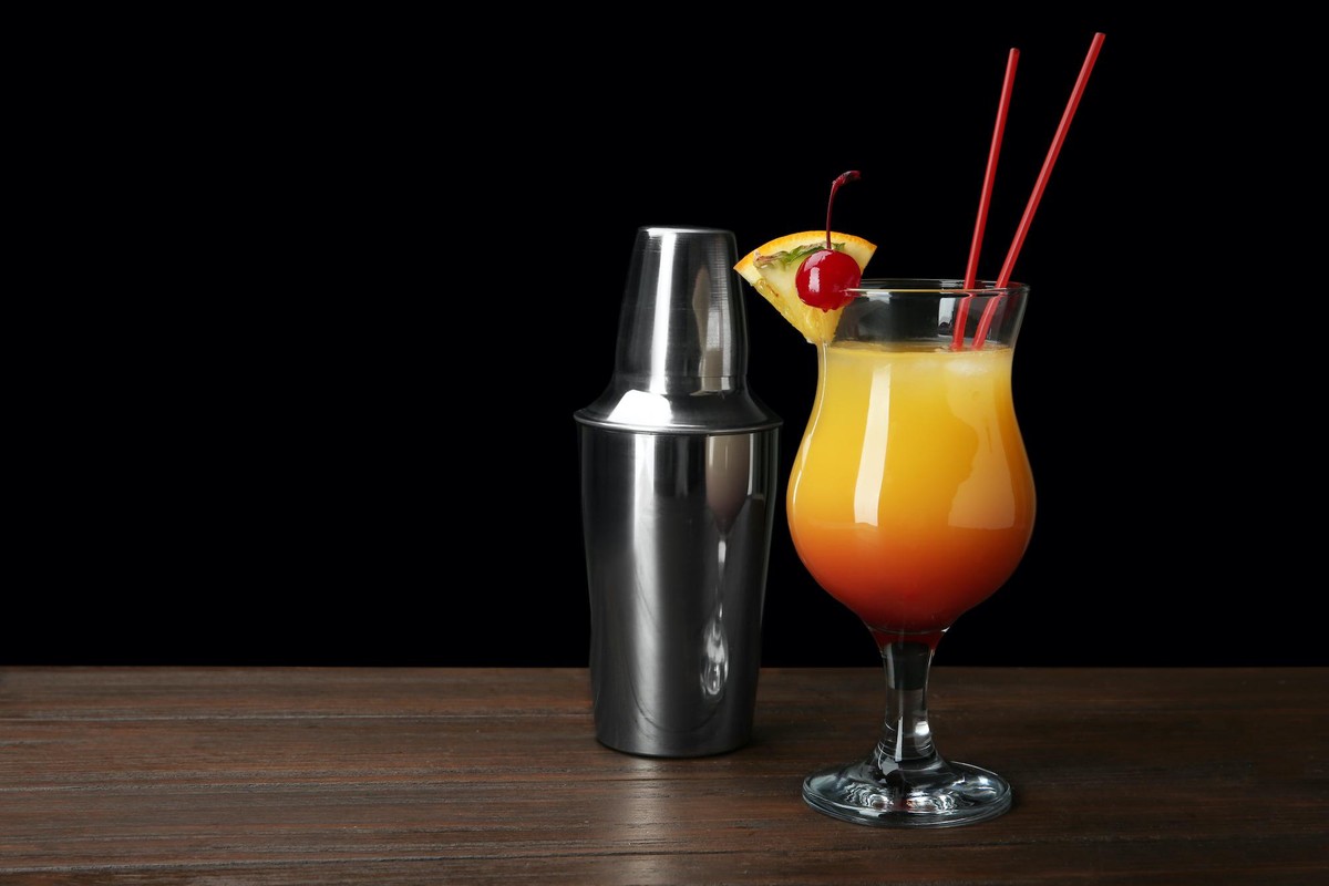 Glass of Sex on the Beach cocktail and shaker against dark background