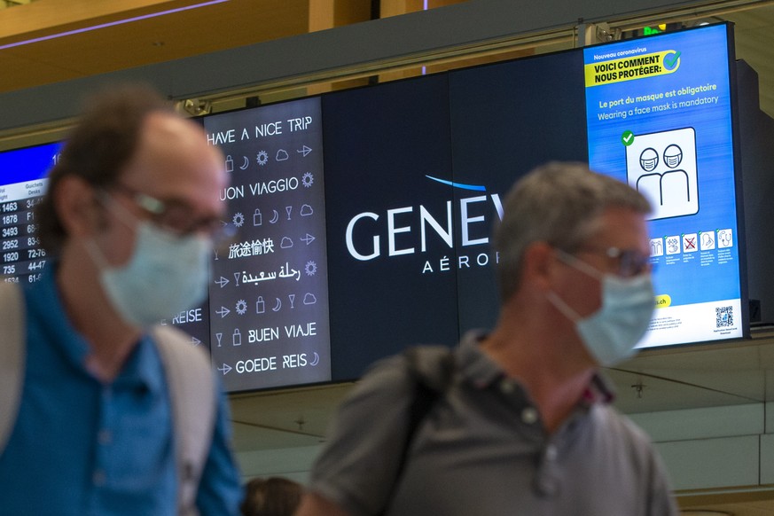 Passengers wearing face masks to protect of the COVID-19 passe in front of a information screen reading &quot;Wearing a face mask is mandatory&quot; to fight against the spread of coronavirus COVID-19 ...