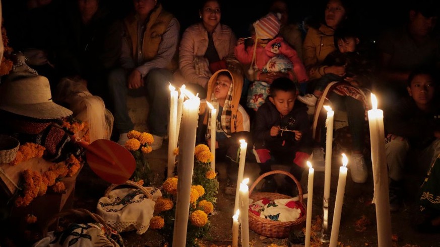 A family in front of a cover with cempasúchil flowers in a community pantheon on Janitzio Island located in the State of Michoacán, Mexico, where residents visited said pantheon to place candles, cove ...