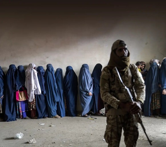 Frauen stehen in Kabul an, um bei einer Hilfsorganisation essen zu holen. Dabei werden sie von einem Taliban-Kämpfer bewacht.