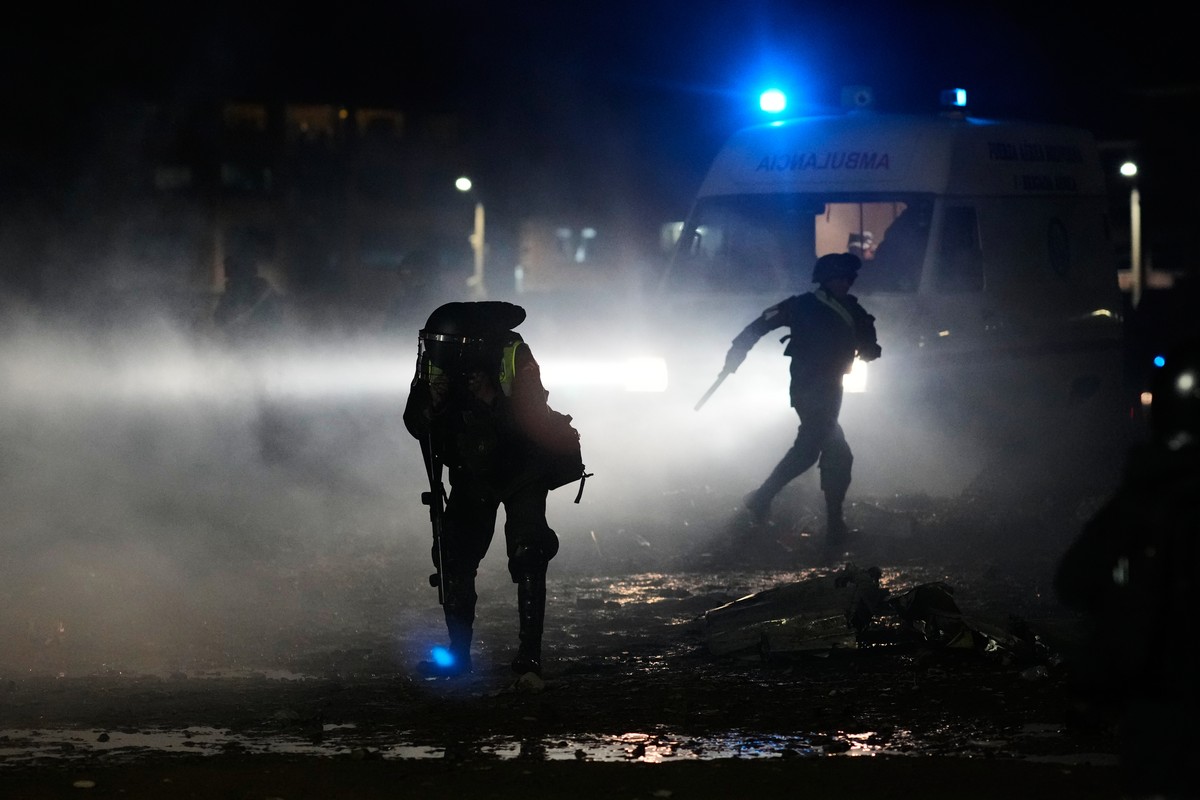 A police covers himself from tear gas spread to disperse people from getting near the area where a aircraft that was transporting money crashed on a highway, in El Alto, Bolivia, Friday, Feb. 27, 2026 ...