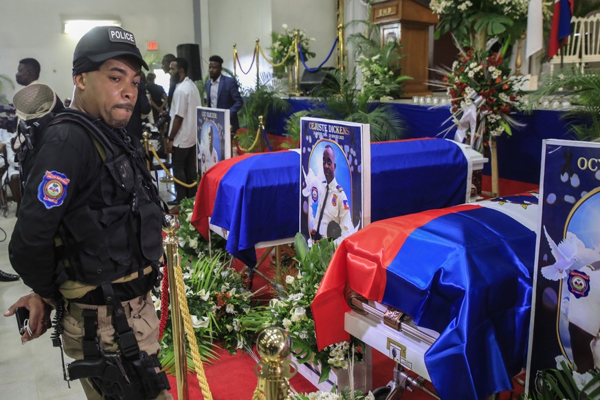 A police officer cries next to coffins containing the bodies of three police officers killed in the line of duty, at the Police Academy in Port-au-Prince, Haiti, Tuesday, Jan. 31, 2023. The officers w ...