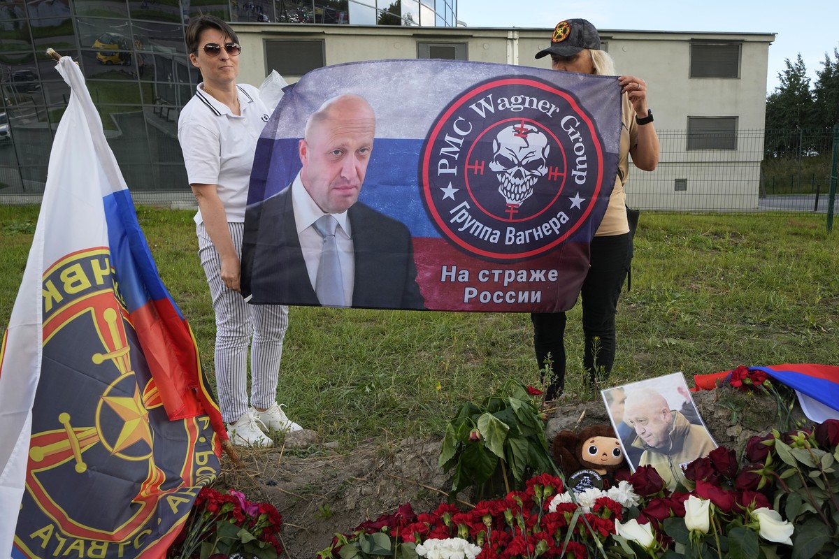 Women hold a flag with an image of the owner of private military company Wagner Group Yevgeny Prigozhin at an informal memorial next to the former 'PMC Wagner Centre' in St. Petersburg, Russ ...