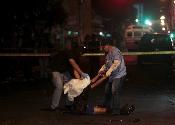 Ein Polizist und ein Forensiker stecken in El Salvador ein Opfer in einen Leichensack.