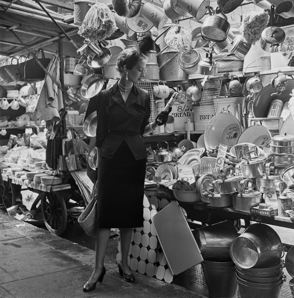 A young woman examining a Flit gun insecticide sprayer by a kitchenware stall at a street market, August 1950. She is modelling a green and bronze shot taffeta jacket, decorated with jet, by Matita. H ...