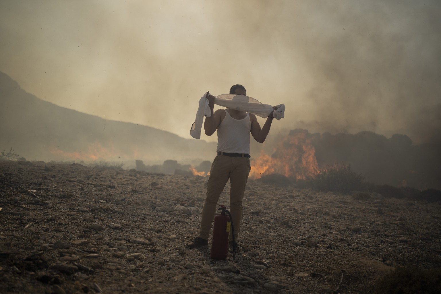 A man wraps his shirt over his face as he tries to extinguish a fire, near the seaside resort of Lindos, on the Aegean Sea island of Rhodes, southeastern Greece, on July 24, 2023. (AP Photo/Petros Gia ...