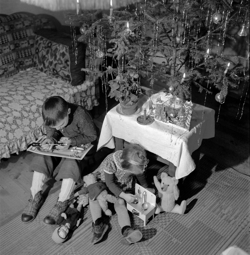 Ein Maedchen und ein Junge spielen unter dem geschmueckten Weihnachtsbaum mit ihren Geschenken, aufgenommen am 25. Dezember im Kriegsjahr 1942, geschlechtertypisch das Maedchen mit einem Kinderkochher ...