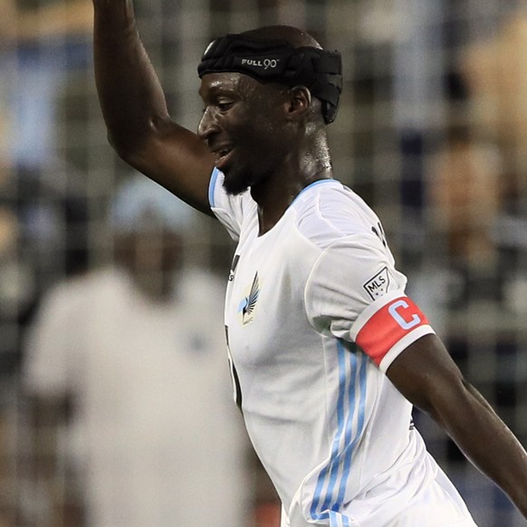 Minnesota United defender Ike Opara (3) steps over Sporting Kansas City forward Daniel Salloi during the first half of an MLS soccer match in Kansas City, Kan., Thursday, Aug. 22, 2019. (AP Photo/Orli ...