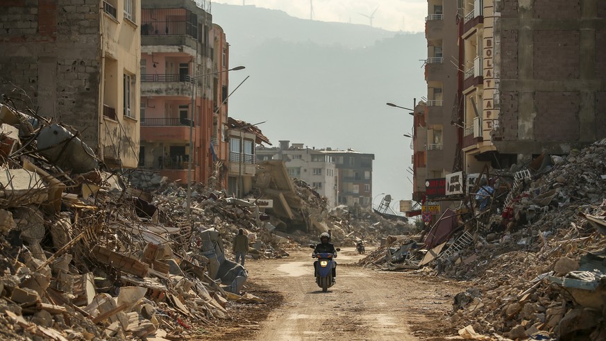 A man rides a motorcycle past debris from destroyed buildings in Samandag, southern Turkey, Wednesday, Feb. 22, 2023. Survivors of the earthquake that jolted Turkey and Syria 15 days ago, killing tens ...