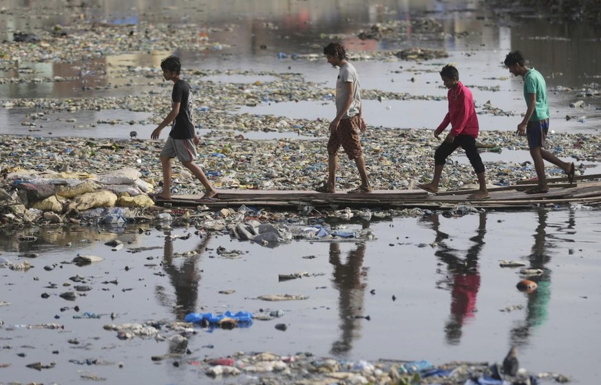 Eine Gruppe spaziert durch einen verschmutzen Wasserkanal in Mumbai, Indien.