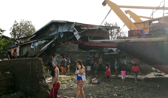epaselect epa08089584 Villagers walk around a cargo ship washed ashore and a damaged home on Christmas day in the typhoon-hit city of Ormoc, Philippines, 25 December 2019. Typhoon Phanfone, (locally k ...