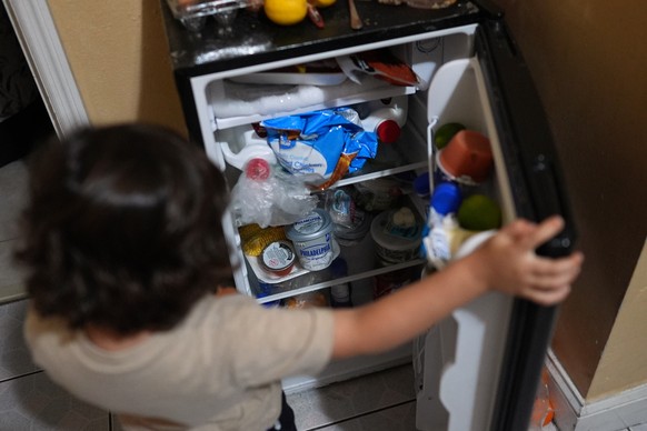 Jakelin Pasedo's three-year-old son hunts for a snack in the mini fridge in the Miami-area motel room where Pasedo is living with her two children, who all have refugee status, Wednesday, Oct. 22 ...