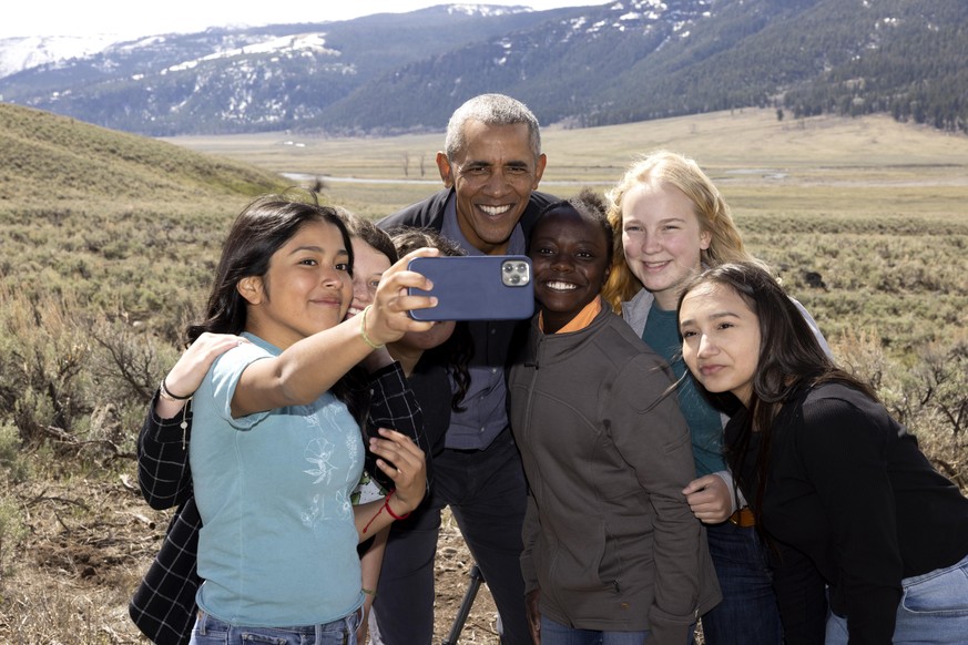 President Barack Obama poses for a cell phone selfie photo with six children in front of a snow-capped mountain range in Yellowstone National Park in Wyoming in “Our Great National Parks.