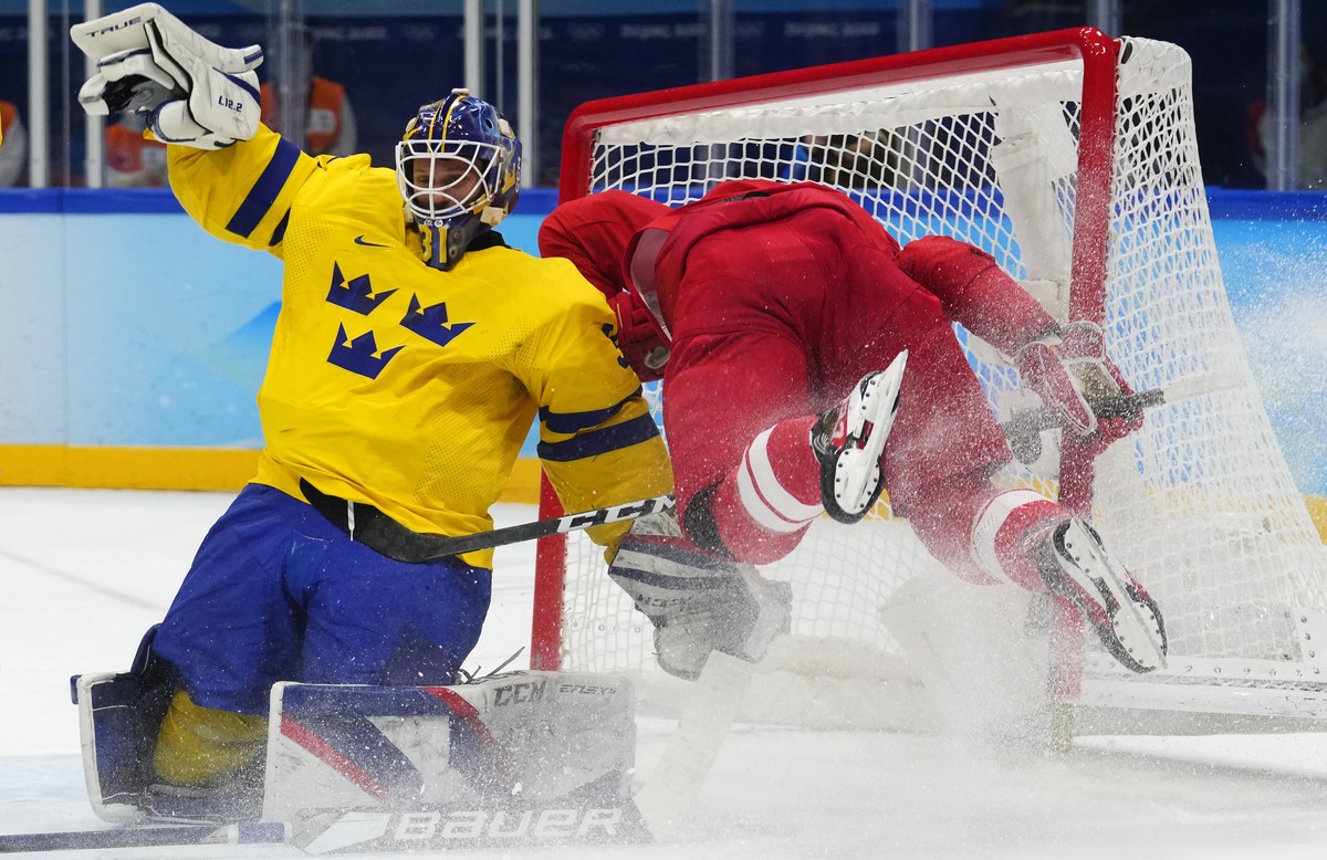 Russian Olympic Committee's Pavel Karnaukhov, right, falls after colliding with Sweden goalkeeper Lars Johansson during overtime in a men's semifinal hockey game at the 2022 Winter Olympics, ...