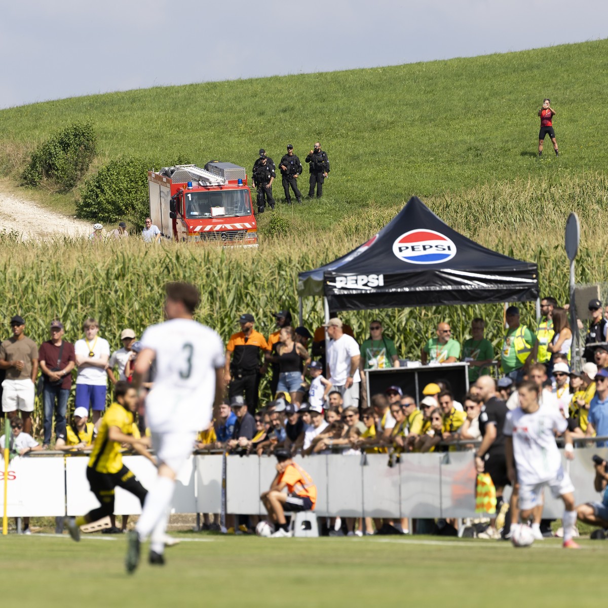 Zuschauer ausserhalb des Stadions verfolgen das Schweizer Cup Spiel in der ersten Hauptrunde zwischen dem FC Courtetelle und dem BSC Young Boys, am Sonntag, 17. August 2025 im Centre Sportif in Courte ...
