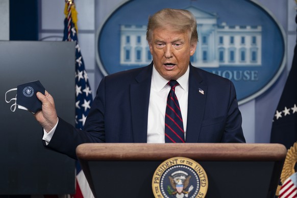 In this July 21, 2020, file photo, President Donald Trump holds a mask as he speaks during a news conference at the White House in Washington. President Trump and first lady Melania Trump have tested  ...