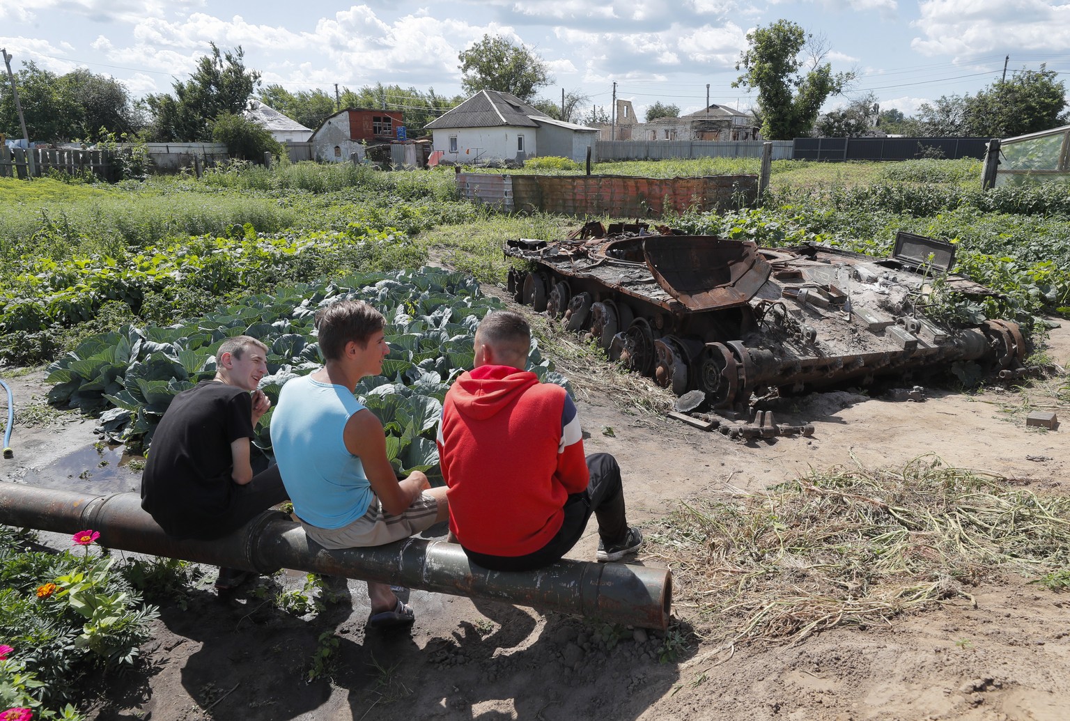 epa10086502 Young local Denis and his friends sit on the debris of a Russian tank in the village of Velyka Dymerka, Kyiv area, Ukraine, 22 July 2022. The wreckage of the tank remained in the garden af ...