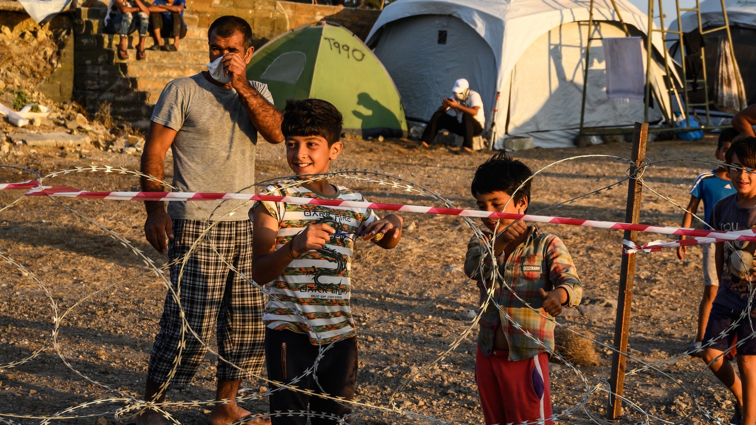 epa08682489 Adults and minors refugees and migrants stand behind razor wire at Kara Tepe camp on Lesbos island, Greece, 19 September 2020. Following the catastrophic fires at Moria on September 8 and ...